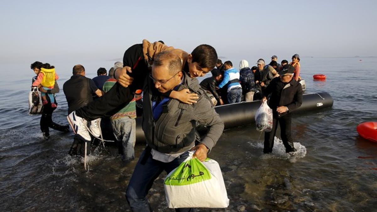 Un refugiado sirio llegado de Turquía carga con un niño en la isla griega de Kos