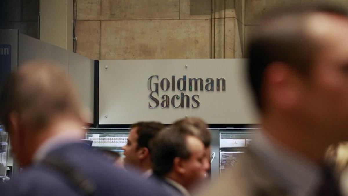 Varios 'brokers' pasan por delante del logo de Goldman Sachs en la Bolsa de Nueva York.