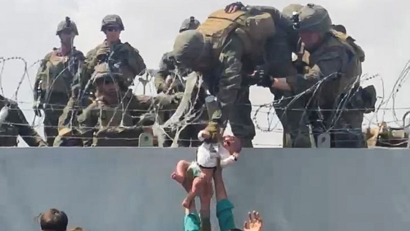 Un bebé sujetado por miembros del ejército americano supera el perímetro del muro del aeropuerto de Kabul