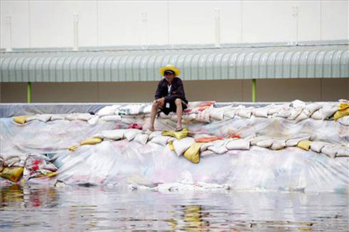 Un home està assegut sobre un munt de sacs de sorra a la inundada província tailandesa de Pathum Thani.