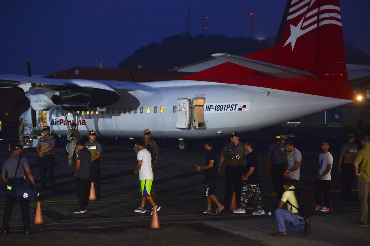 Migrantes colombianos esposados entran en un avión en Panamá para ser deportados a Colombia.