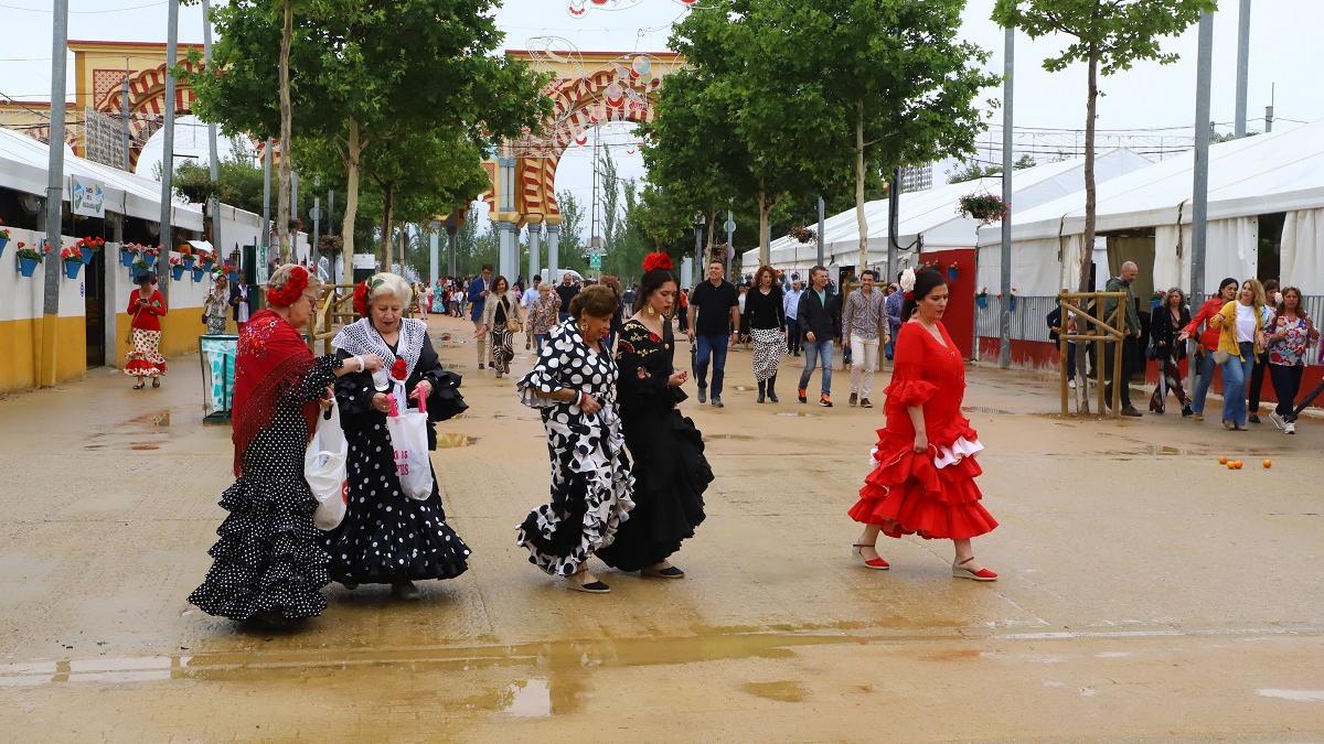 Un grupo de mujeres con traje de flamenca sortean los charcos en El Arenal durante la Feria de Córdoba, que se celebra esta semana.