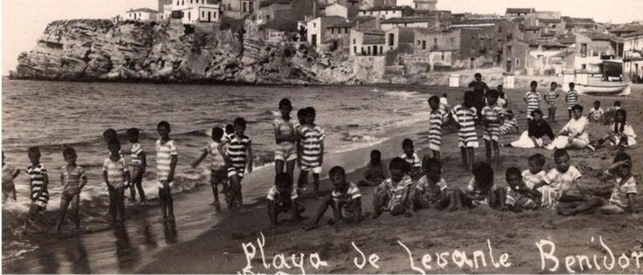 Un numeroso grupo de niños, junto a varias mujeres, disfrutan de la playa de Levante de Benidorm, muy cerca del Torrejó, en una imagen de principios del pasado siglo que se conserva en el Archivo Municipal.