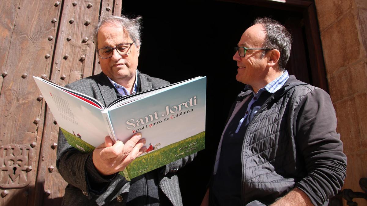 L' expresident de la Generalitat, Quim Torra, i el fotògraf Òscar Rodbag fullejant el seu llibre "Sant Jordi, heroi i patró de Catalunya" a les portes de l'església de Sant Maria de Montblanc