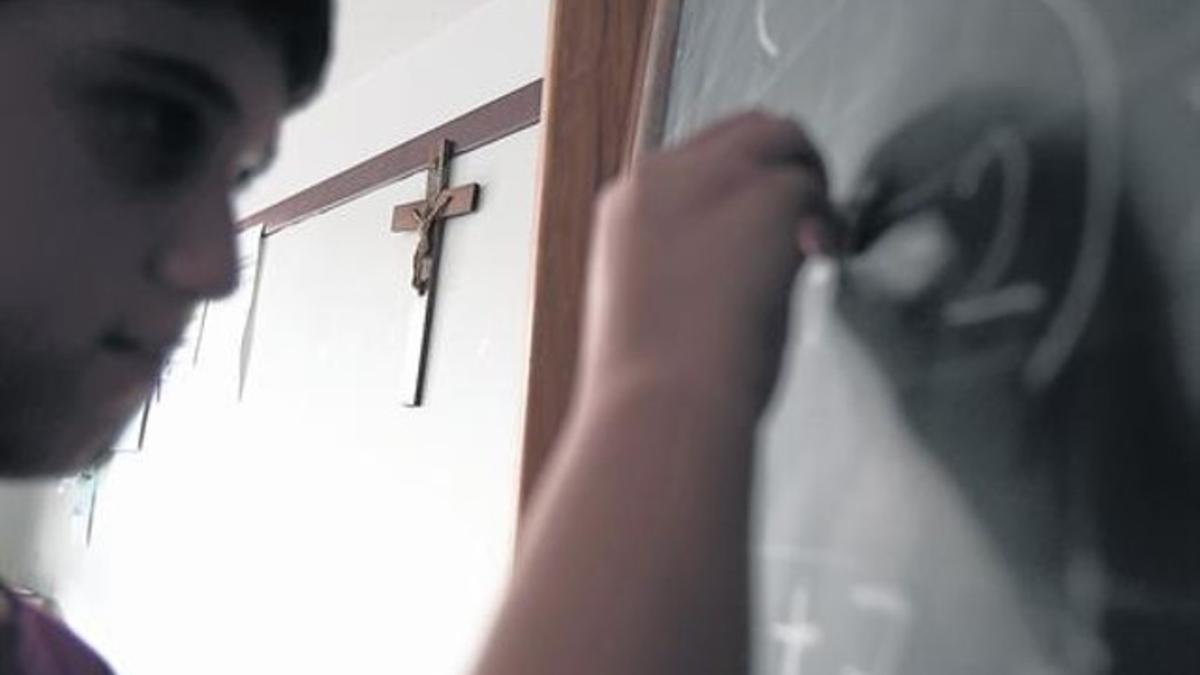 Un alumno de una escuela religiosa escribe en la pizarra junto a un crucifijo colgado en la pared del aula.