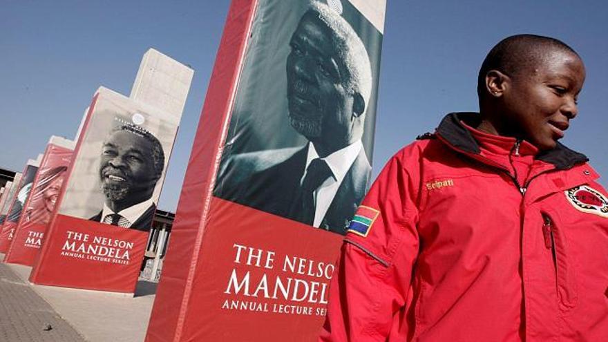 Un guía turístico aparece junto a varios pósters de personalidades importantes relacionadas con Nelson Mandela en la Plaza Walter Sisulu en Soweto, Johanesburgo, Sudáfrica, hoy jueves 17 de julio. Estos pósters se han colocado como parte de las celebraciones del 90 cumpleaños de Mandela.