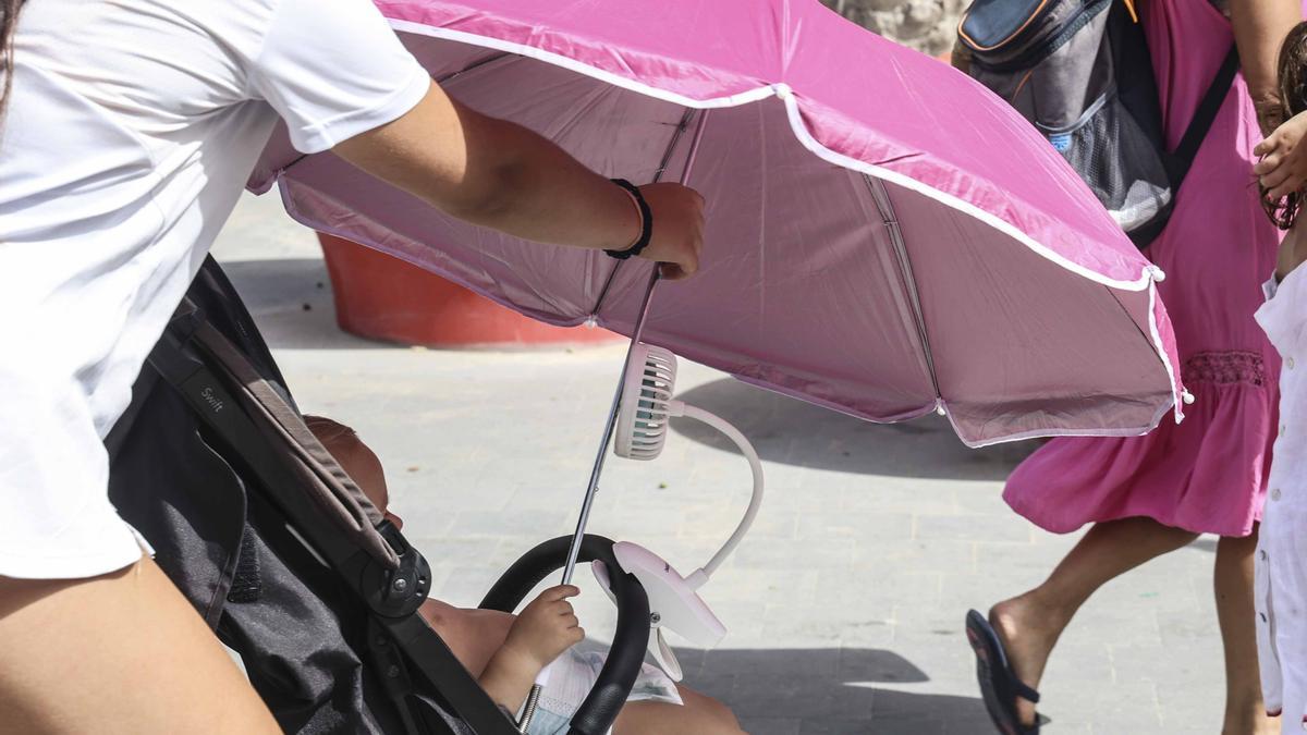 Un bebé protegido con una sombrilla y un ventilador en Alicante