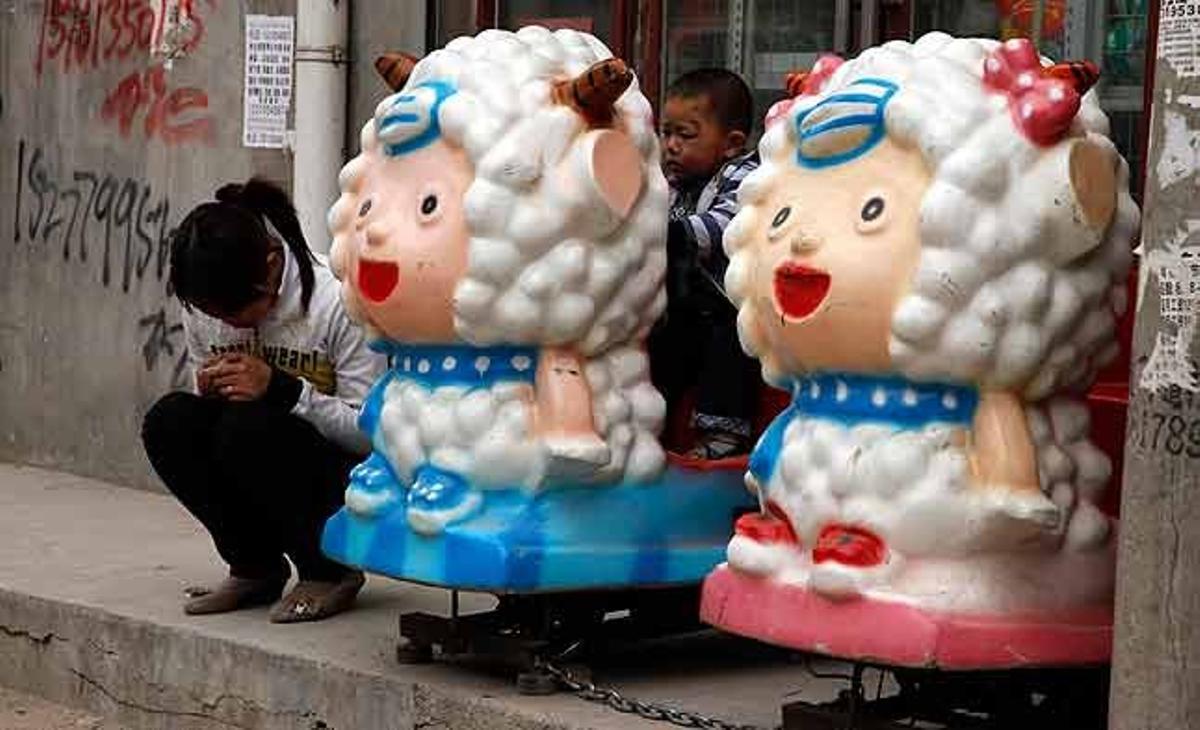 Un nen juga sobre un ninot mecànic al costat d’una dona, en un carrer del districte de Daxing, a Beijing (Xina).