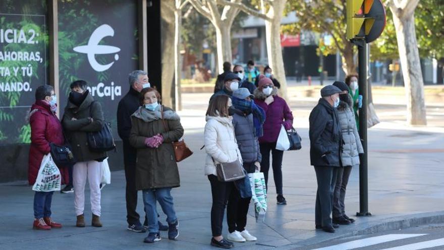 Varias personas esperan en un paso de peatones de la plaza Aragón, en Zaragoza.