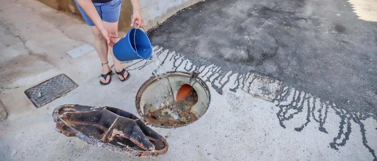 Una vecina echa agua en una de las alcantarillas donde se quedan acumulados residuos fecales provocando mal olor.