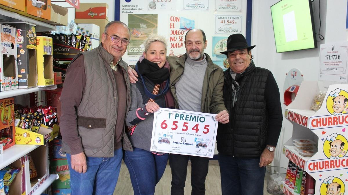 Félix Pérez, el dueño del estanco y punto de venta de loterías que ha dado el premio en El Carpio, junto a varios clientes y amigos, con el cartel del número premiado.