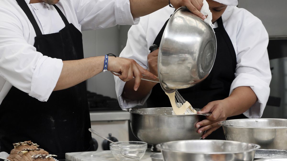 Dos reposteros preparan un pastel en una cocina.