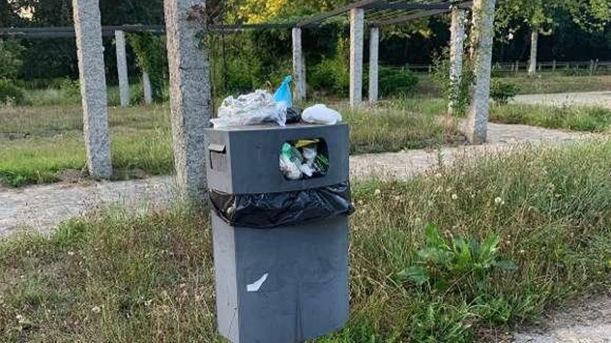 Papelera llena de basura al lado de la pérgola del paseo.