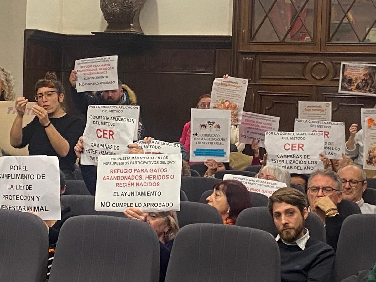 Personas en el pleno con carteles de protesta.