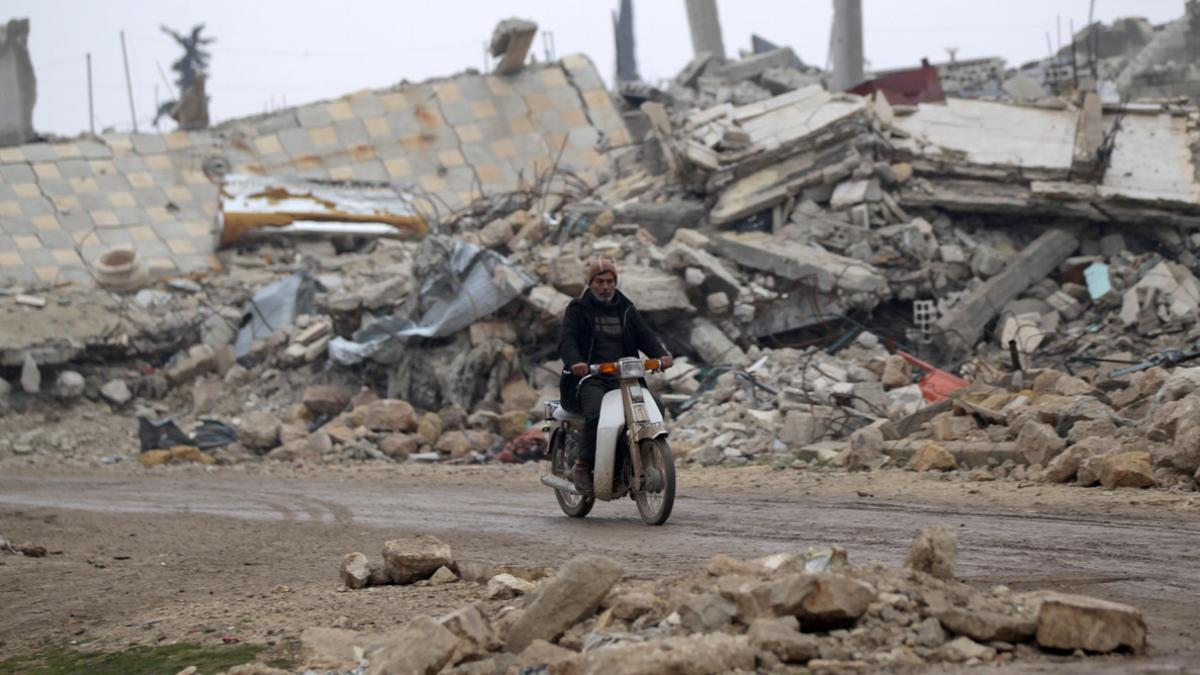 A man drives a motorcycle near rubble of damaged buildings in al-Rai town