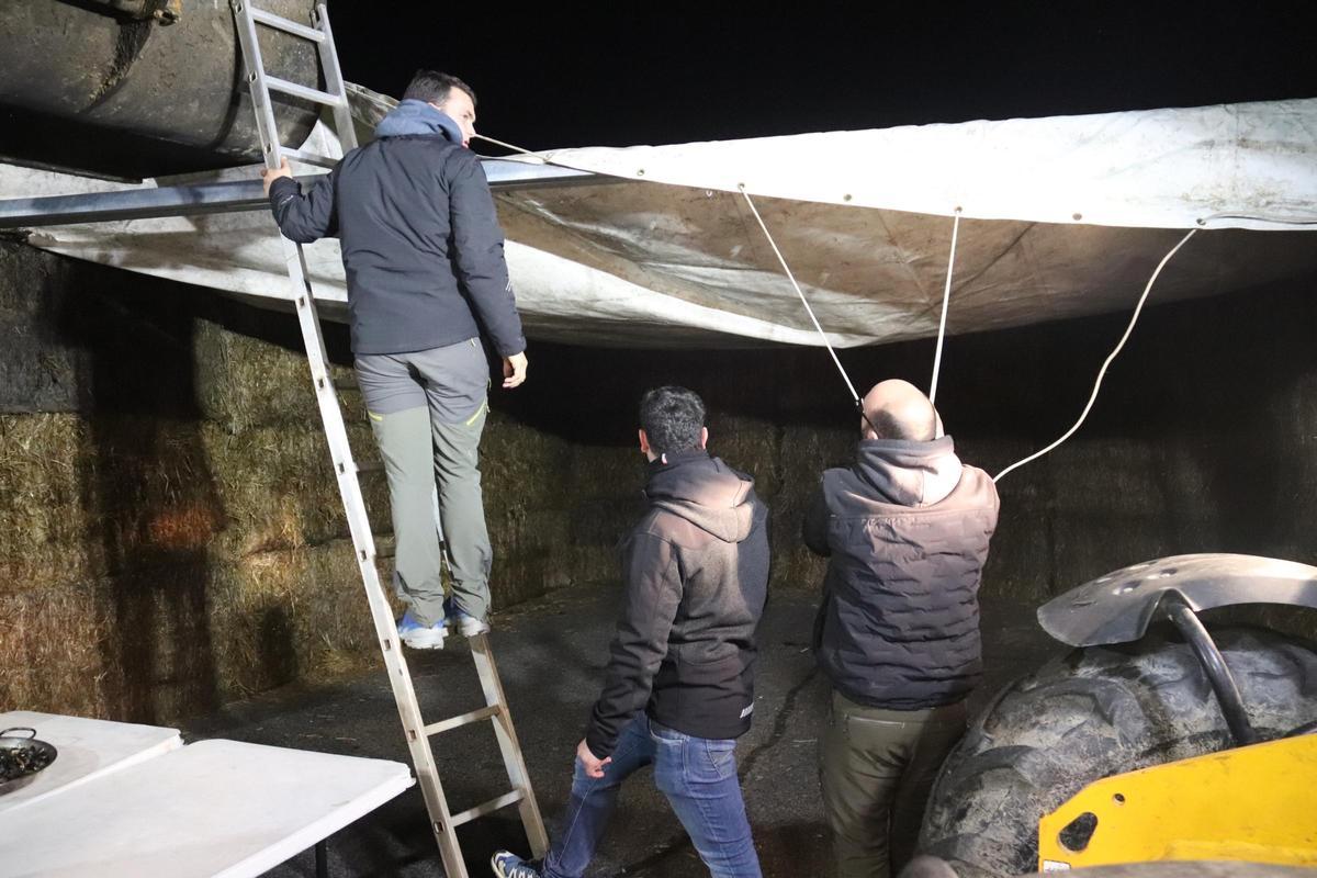 Uns pagesos estiren una tela per fer un cobert sobre bales de palla en el tall de l'AP-7 a Pontós