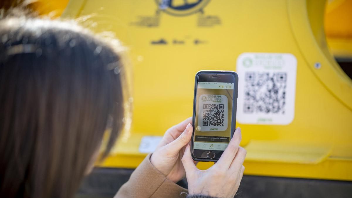 Una chica escanea el código QR de un contenedor amarillos antes de reciclar sus envases