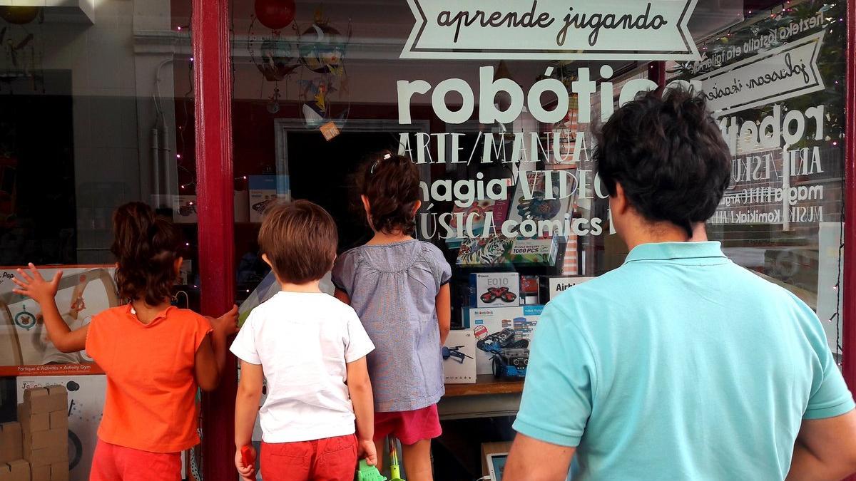 Un padre mira con sus hijos el escaparate de una tienda infantil de robótica