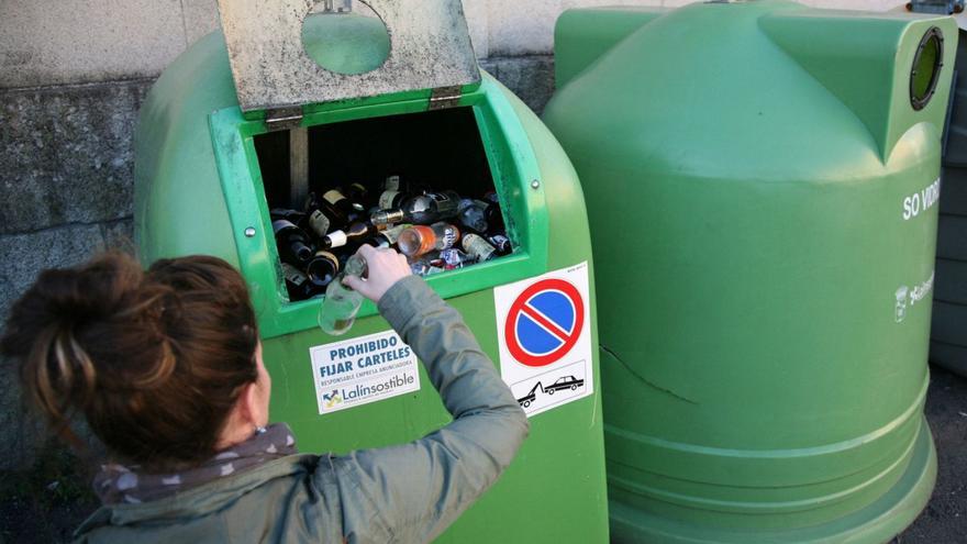 Una persona tira una botella de vidrio en un contenedor verde, en Lalín.
