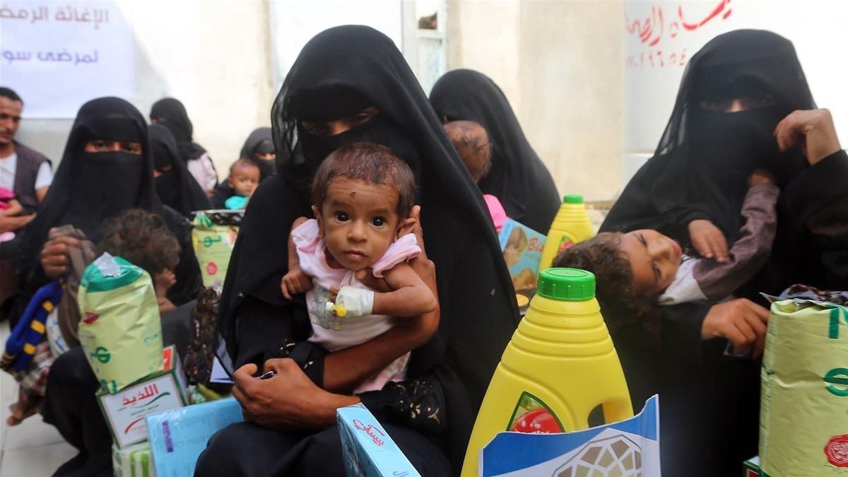 Mujeres yemenís sostienen a sus hijos mientras esperan el reparto de comida en la provincia de Al Hudayda.