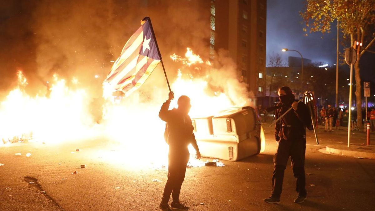 Una persona amb una estelada davant un contenidor cremat en les protestes convocades per Tsunami Democràtic durant el derbi Barça-Madrid. | FERRAN NADEU