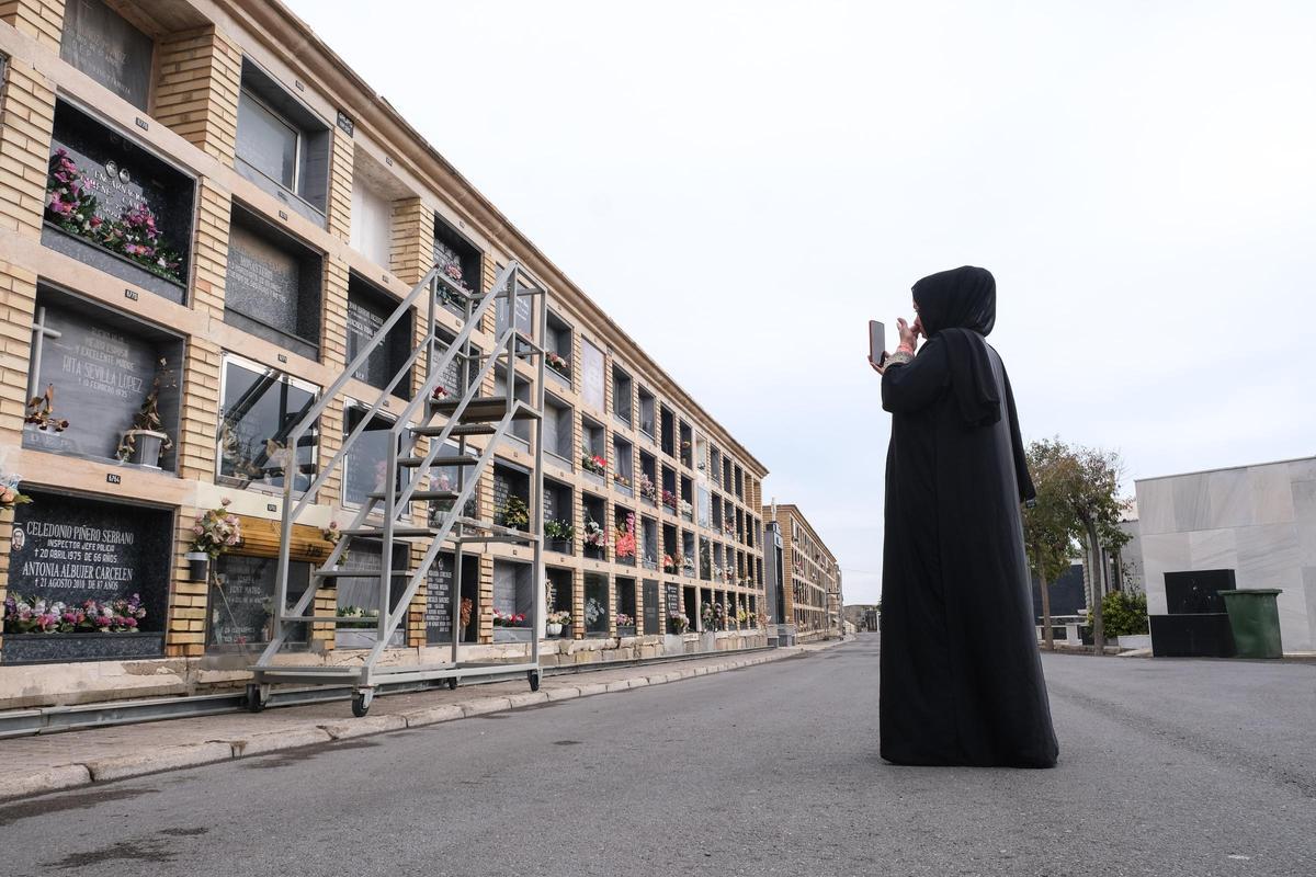 Mina conversa con la madre de un chaval que yace en un nicho sin nombre (arriba a la  izquierda) en el cementerio de Alicante. La mujer, que le ha reconocido por las fotos de la ropa que llevaba, llora desde  Marruecos. Mina también. Para exhumarle falta  la prueba de ADN.