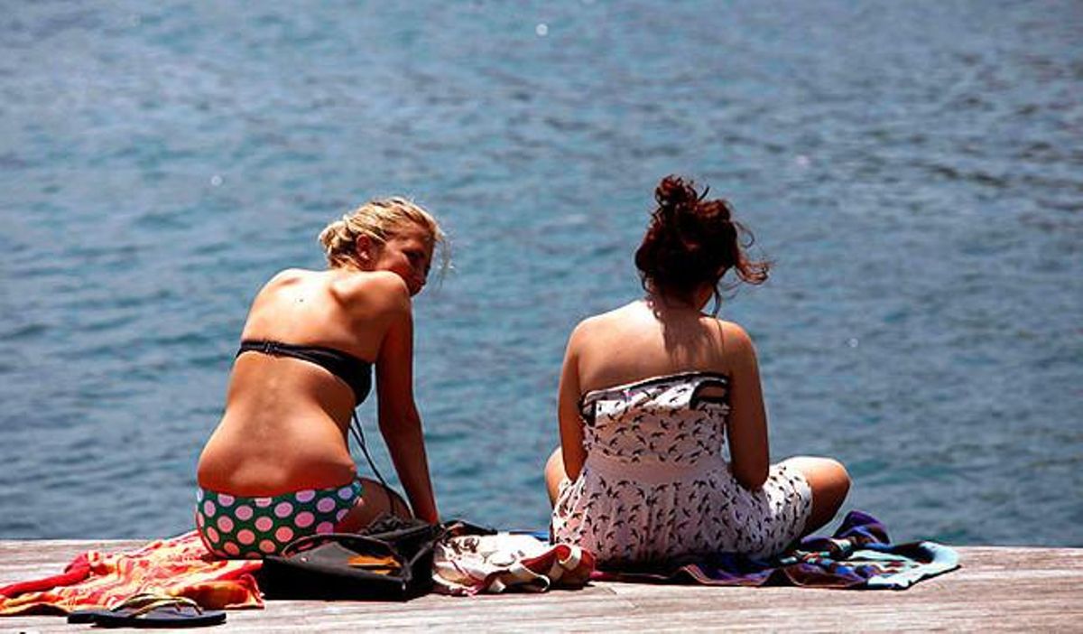 Dos joves turistes aprofiten les elevades temperatures per prendre el sol davant el mar de Barcelona.