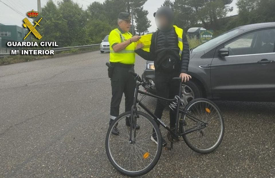 El agente de la Guardia Civil entrega un chaleco reflectante al ciclista