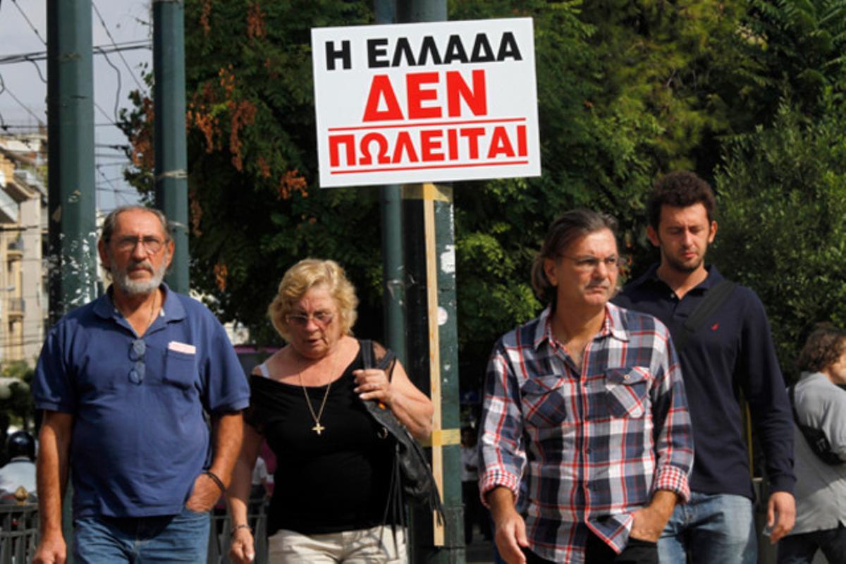 Vianants a Atenes passen pel davant d’un cartell que diu: ’Grècia no està en venda,’ en un dia més de protestes contra les retallades del Govern grec.