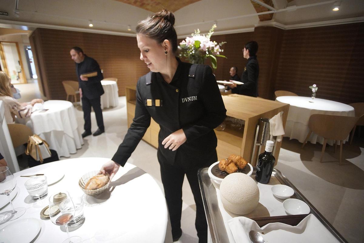 Aina García diposita una plata amb pa en una taula, en lìnici d'un servei de migdia al restaurant Divinum de Girona.