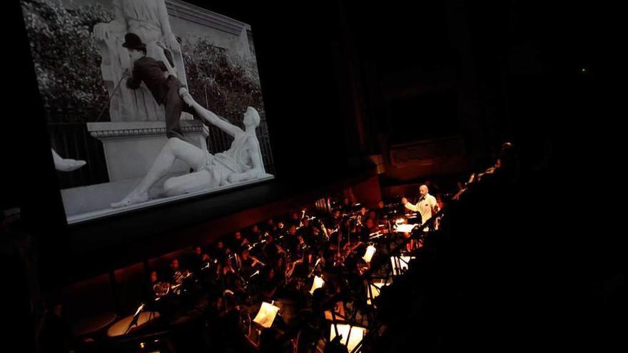 Mariano Rivas dirige a la Orquesta Filarmónica de España en el Jovellanos, mientras en pantalla se proyecta la película de Chaplin &quot;Luces de la ciudad&quot;.