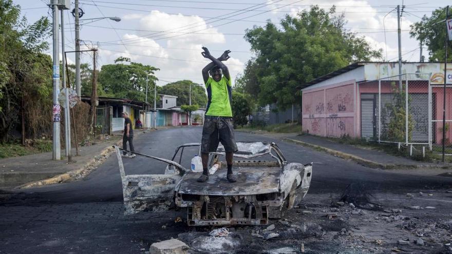 Un hombre protesta encima de un vehículo quemado