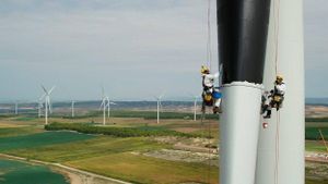 Dos operarios pimtan de negro una pala de un aerogenerador de Iberdrola.