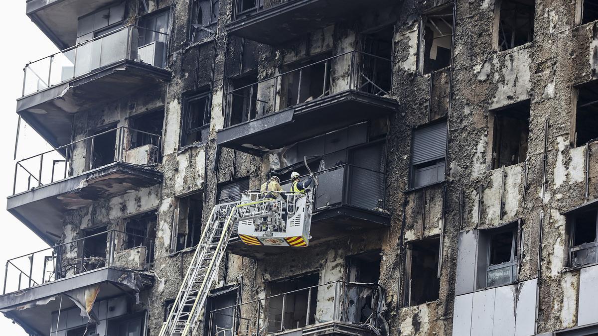 Bomberos en una grúa sanean la fachada quemada del edificio de Campanar