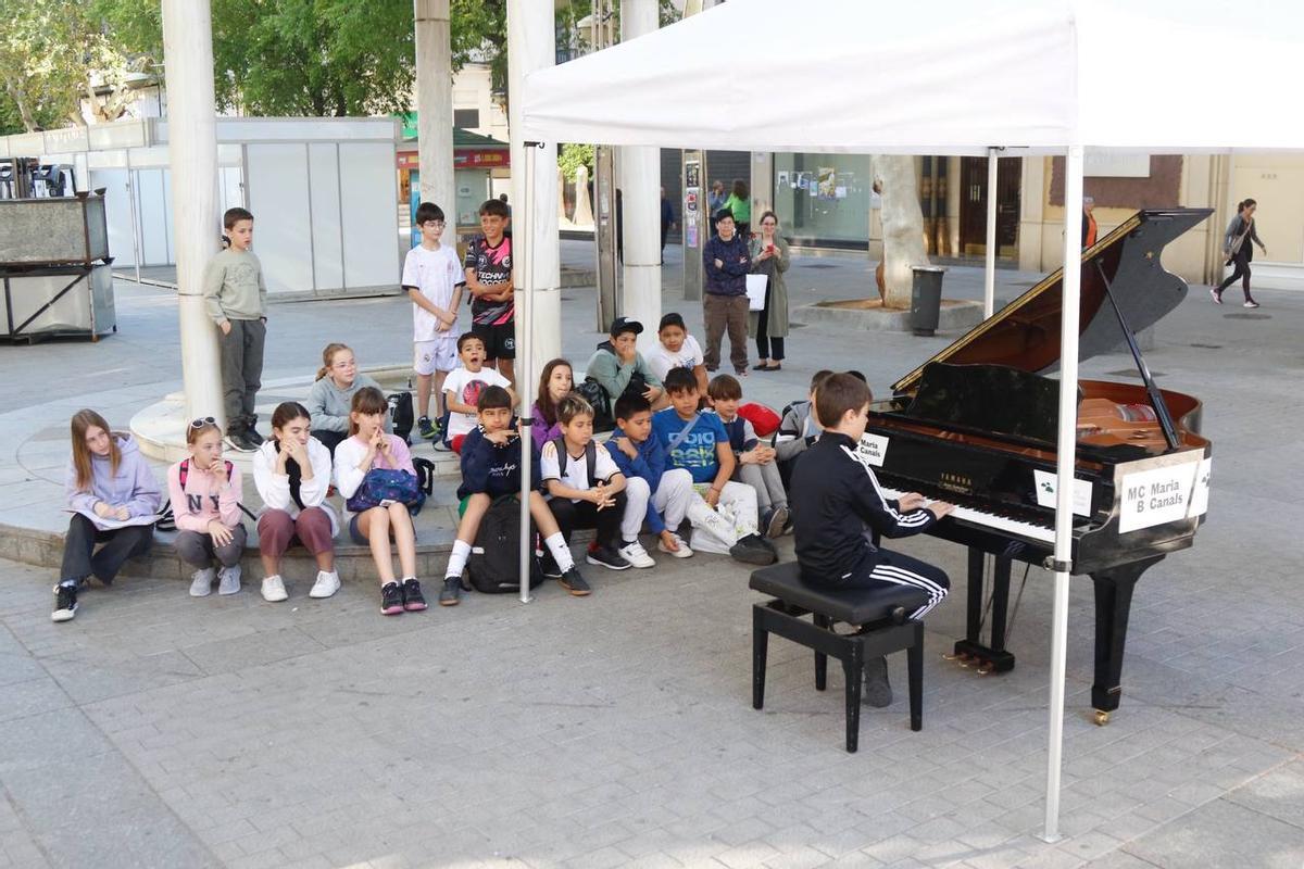 Un niño, rodeado de otros niños, interpreta un tema en el gran piano de cola de Las Tendillas.