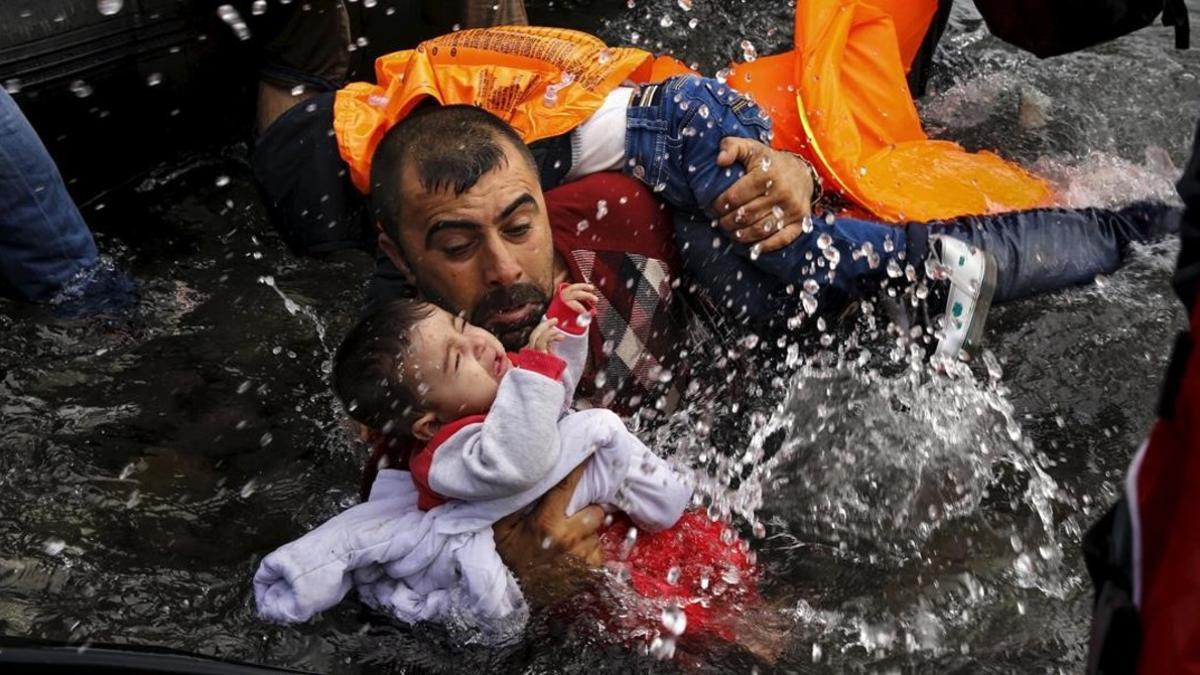 Un refugiado intenta mantener fuera del agua a su hijo pata que no se ahogue frente a la costa de Lesbos.