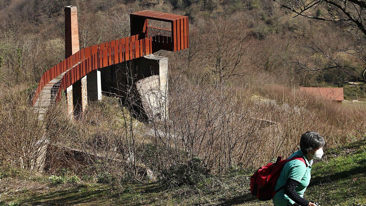 Una senderista pasa junto al mirador del poblado, con la chimenea a la izquierda y las viviendas rehabilitadas al fondo. | Juan Plaza