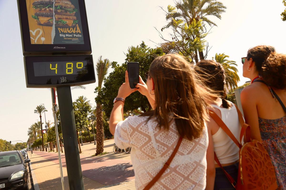 Varias chicas fotografían un termómetro que marca 48 grados en el centro de Córdoba.