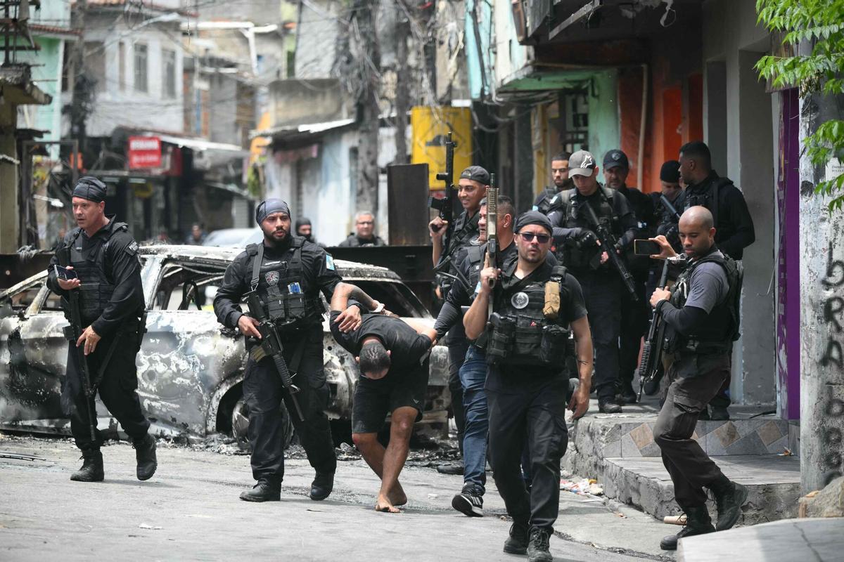 TOPSHOT - Police officers escort a suspect arrested during the Operacao Contencao (Operation Containment) out of the Vila Cruzeiro favela, in the Penha complex, in Rio de Janeiro, Brazil, on October 28, 2025. At least 2,500 security forces agents took part in an operation to arrest drug traffickers from the Comando Vermelho (CV), which resulted in 18 suspects and several police officers dead. (Photo by Mauro PIMENTEL / AFP)