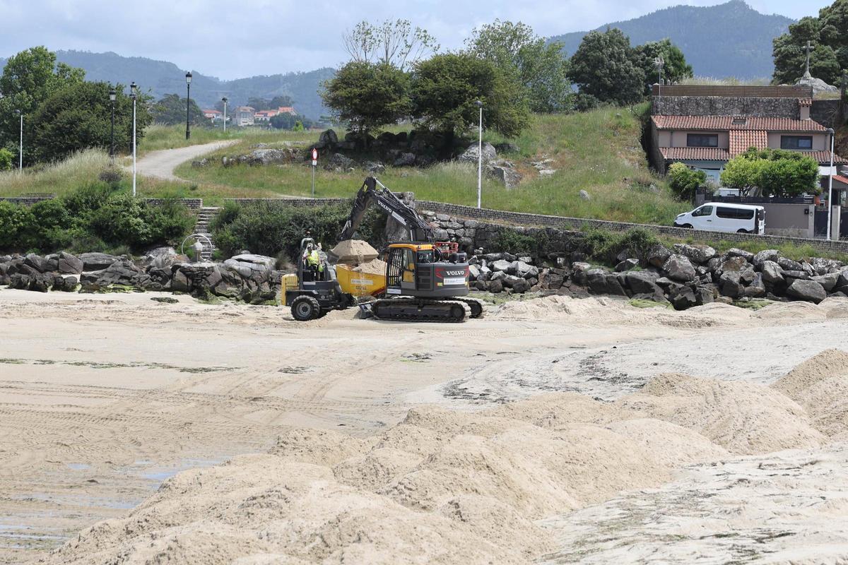La excavadora retira la arena acumulada en la desembocadura del río Baíña para que el volquete la lleve al otro extremo de la playa.