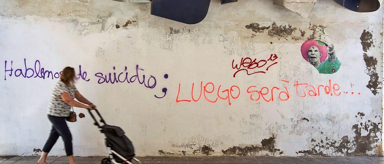Una mujer camina frente a una pintada alusiva al suicidio en la ciudad de Alicante. | ALEX DOMÍNGUEZ