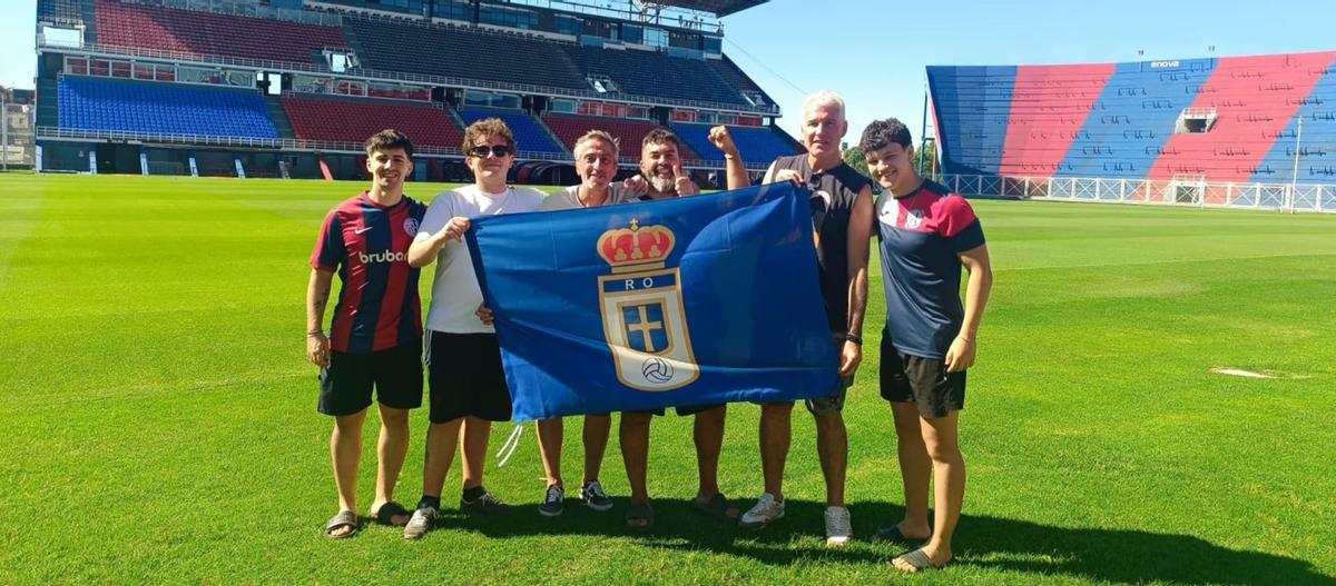 Fernando del Campo, tercero por la izquierda, entre su sobrino Iván y Marcelo Alejandro Fernández, despliega la bandera del Oviedo en el campo de San Lorenzo de Almagro con la ayuda de Javier Enrique Agustín y los hijos de Marcelo. | LNE