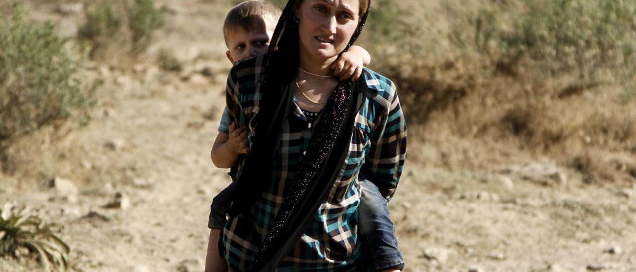 Una mujer yazidí, con su hijo a la espalda, cruza la frontera con Turquía, en 2014. // EFE