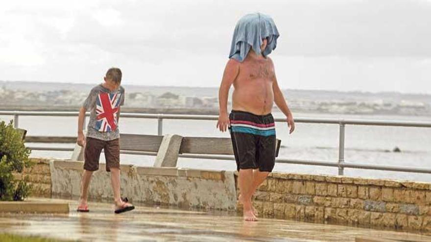 Turistas en bañador se intentan cubrir de la lluvia de ayer.