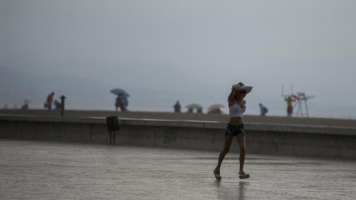 Una joven se protege de la lluvia en la playa del Fòrum, en Barcelona.