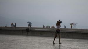 Una joven se protege de la lluvia en la playa del Fòrum, en Barcelona.