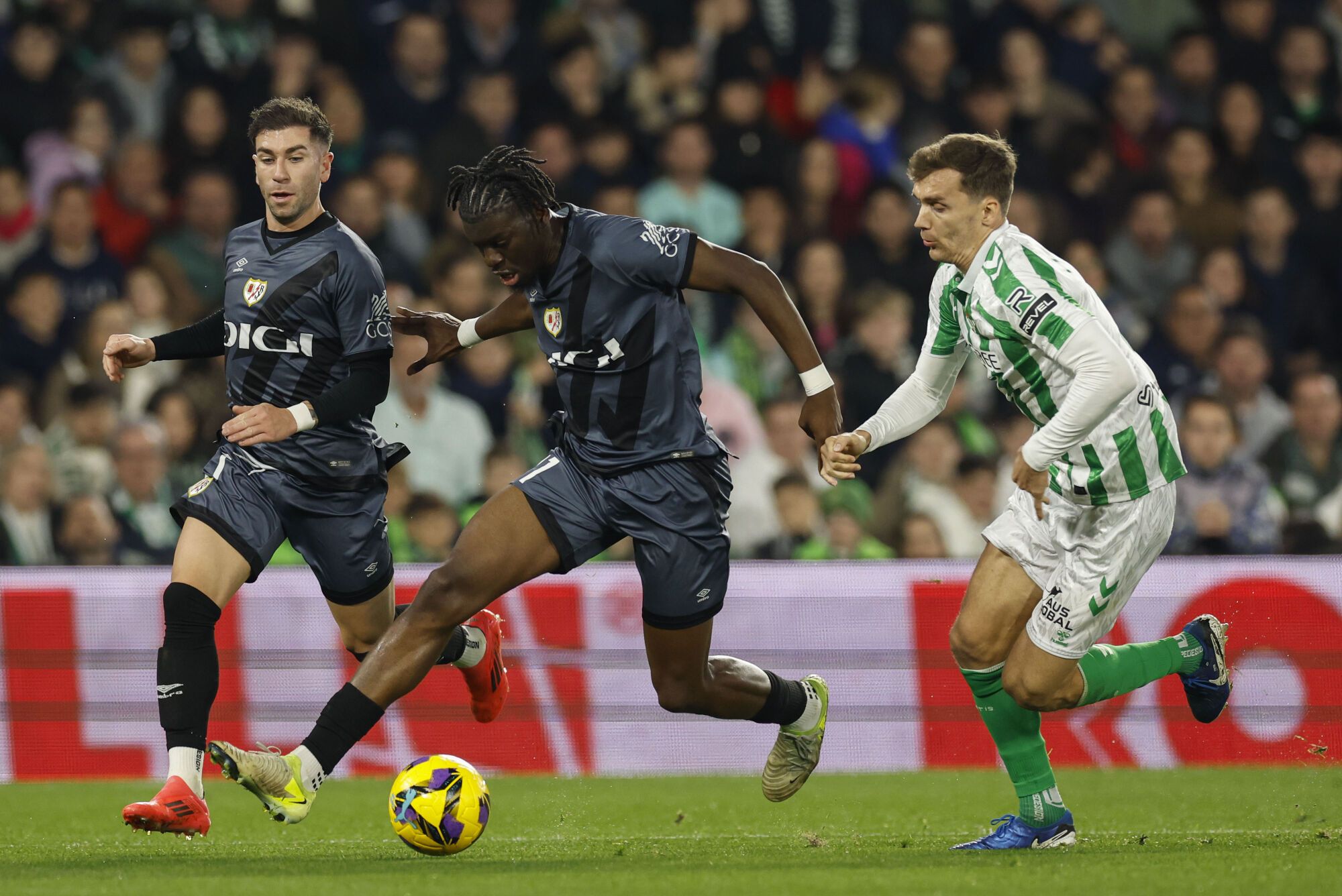 SEVILLA, 22/12/2024.- El delantero angoleño del Rayo Randy Nteka (c) se escapa de Diego Llorente, del Betis, durante el partido de la jornada 18 de LaLiga EA Sports disputado este domingo entre el Real Betis y el Rayo Vallecano en el estadio Benito Villamarín de Sevilla. EFE/ Julio Muñoz