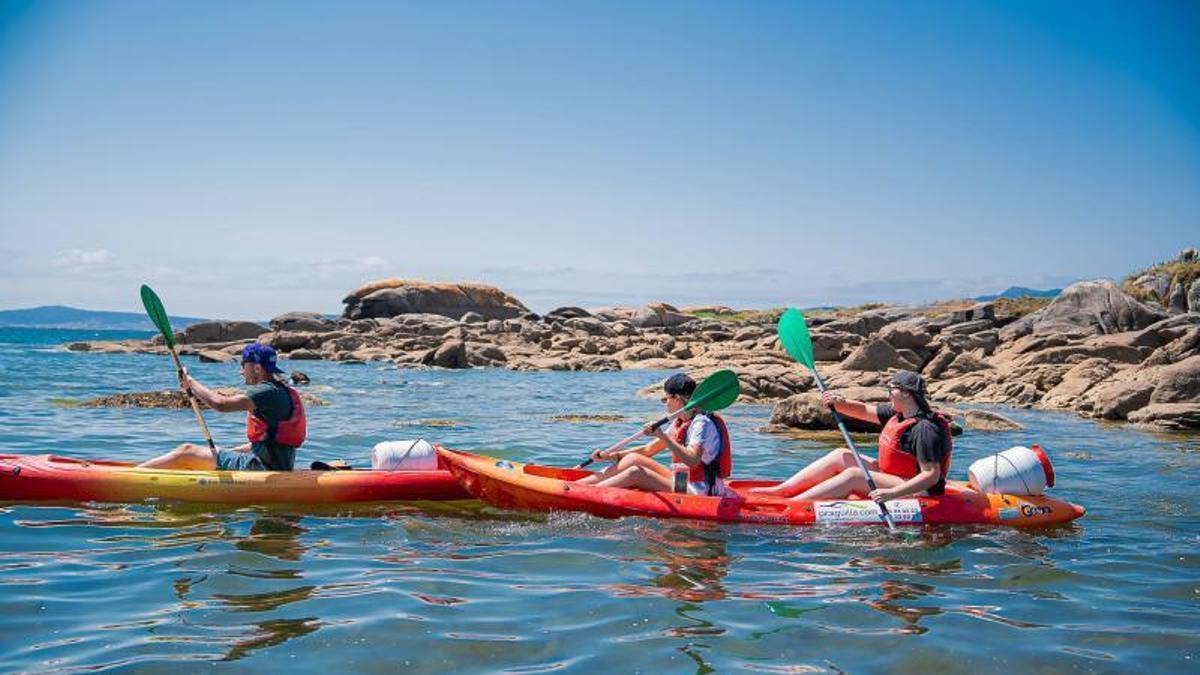 Tres kayaks parten desde A Illa hacia Areoso.