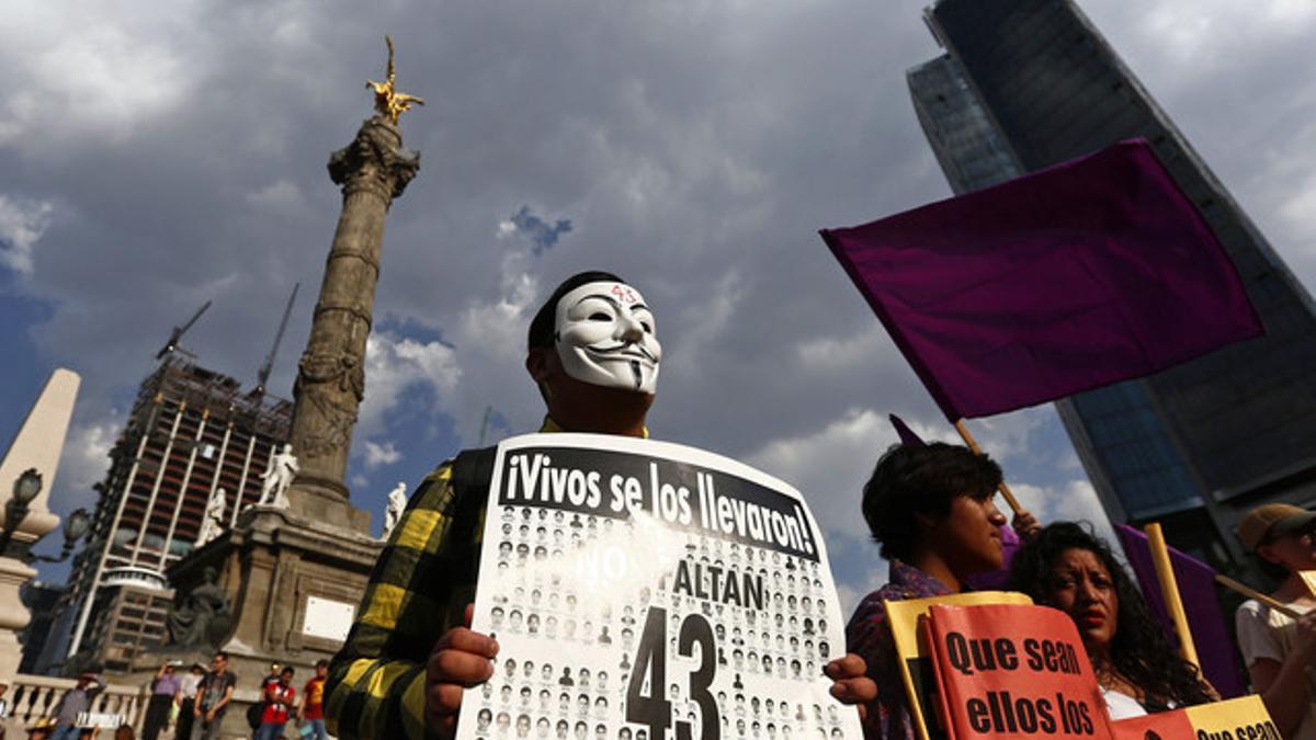A protester in a Guy Fawkes mask holds a sign during a march to demand justice for the 43 missing students of the Ayotzinapa Teacher Training College, in Mexico City