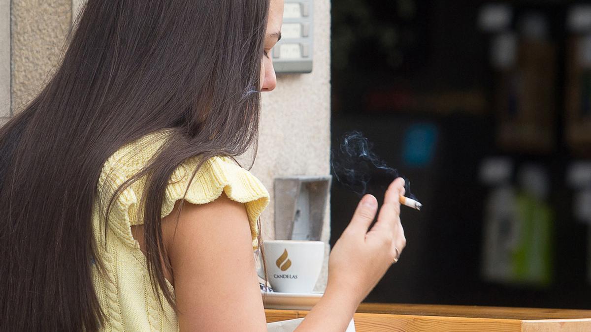 Una mujer fumando en la terraza de un bar.